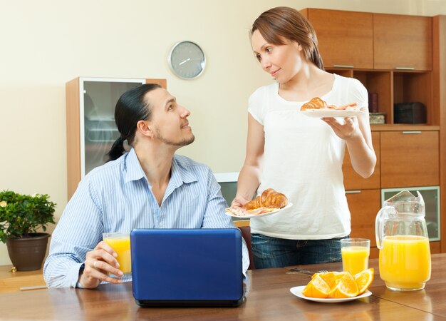 Casal feliz usando o laptop durante o café da manhã