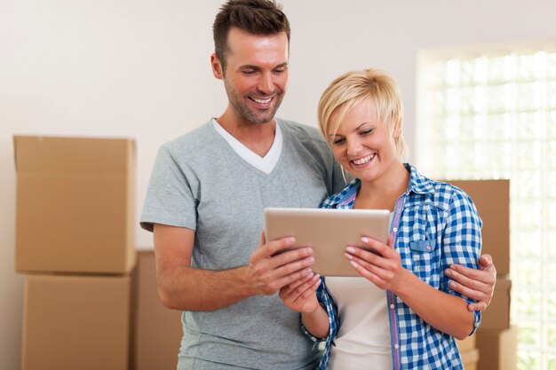 Casal feliz usando tablet digital durante a mudança para casa