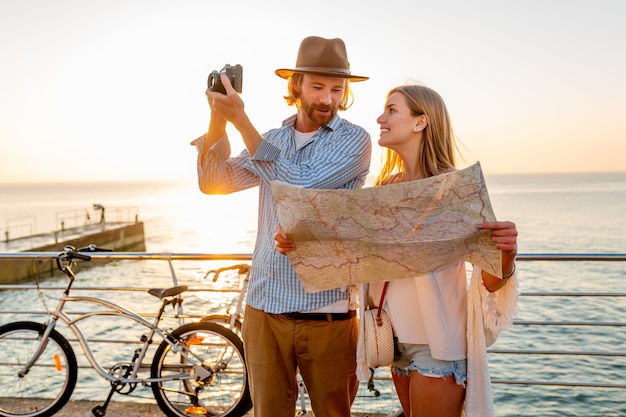 Casal feliz viajando no verão de bicicleta, olhando um mapa e tirando fotos com a câmera