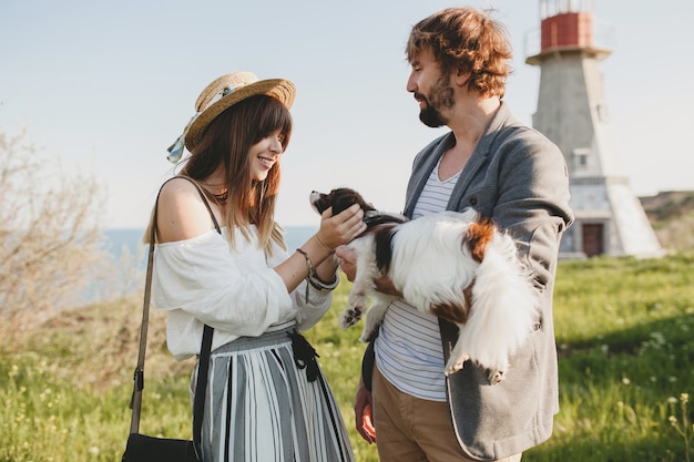 Casal fofo e elegante hippie apaixonado caminhando com um cachorro no campo