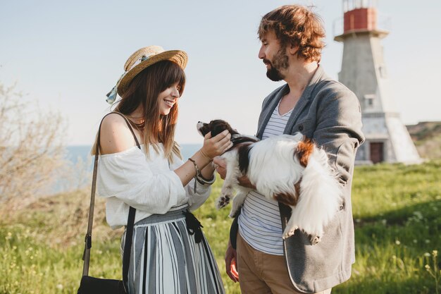 Casal fofo e elegante hippie apaixonado caminhando com um cachorro no campo