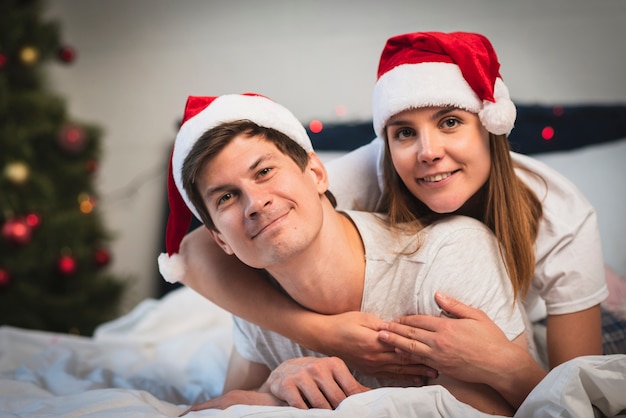 Casal fofo usando chapéus de Papai Noel na cama