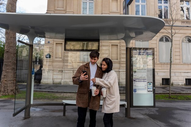Casal francês esperando na estação para pegar o ônibus e usando um smartphone