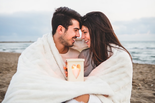 Casal frente para o outro na areia com uma vela e um cobertor