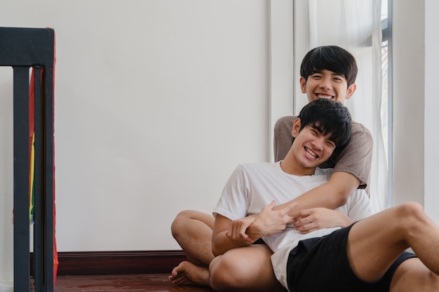 Foto grátis casal gay asiático deitado e abraçando no chão em casa. os jovens asiáticos lgbtq + homens se beijando felizes relaxam o resto juntos passam tempo romântico na sala de estar com a bandeira do arco-íris na casa moderna de manhã.