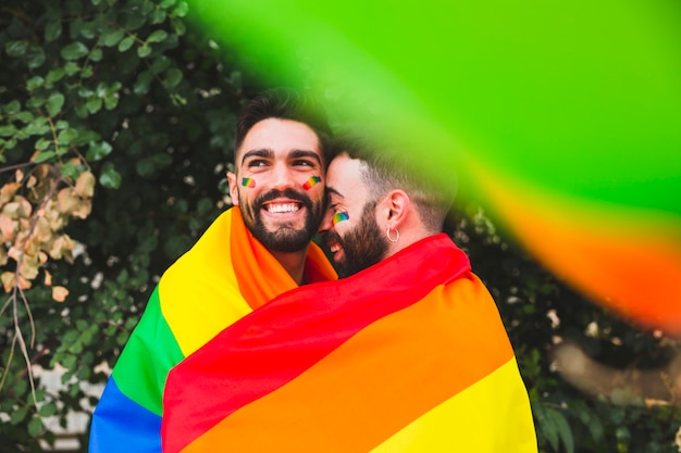 Casal gay com bandeira de arco-íris abraçando na rua