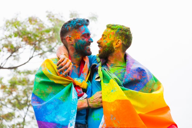 Casal gay com caras pintadas, regozijando-se e abraçando