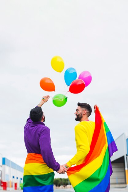 Casal gay liberando balões arco-íris no céu