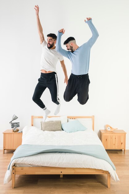 Casal gay pulando na cama no quarto