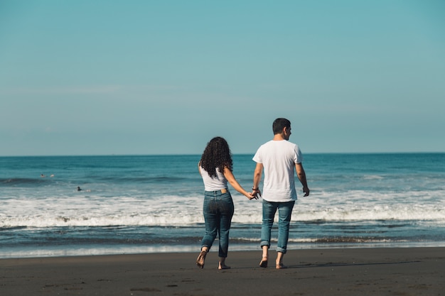 Casal indo descalço na areia para o mar