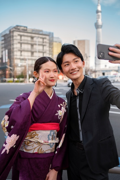 Foto grátis casal japonês comemorando o dia da maioridade ao ar livre tirando uma selfie