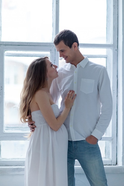 Casal jovem alegre, vestido de branco, sentado no sofá