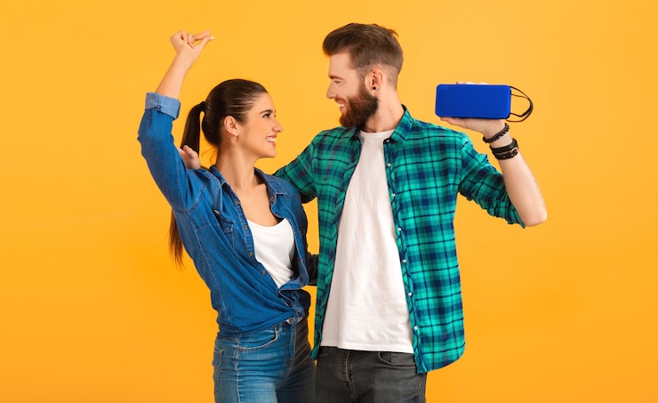 Foto grátis casal jovem casual segurando alto-falante sem fio, ouvindo música dançando estilo colorido, feliz humor isolado em fundo amarelo
