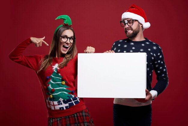 Casal jovem com roupas estranhas de Natal segurando um papel em branco