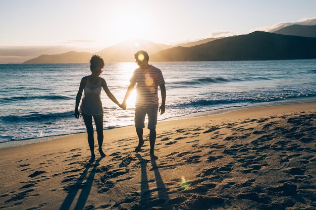 Casal jovem de mãos dadas na praia ao pôr do sol