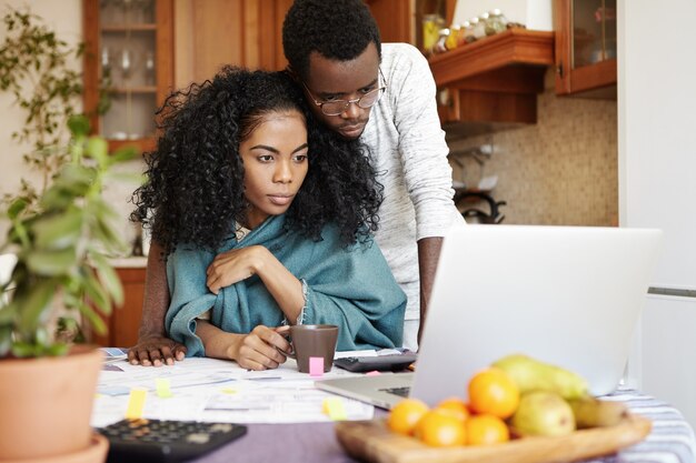 Casal jovem de pele escura usando laptop genérico enquanto gerencia o orçamento familiar