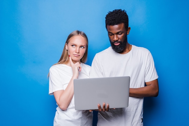 Casal jovem de raça mista segurando laptop isolado na parede azul