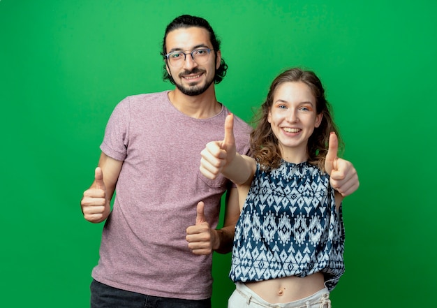 Foto grátis casal jovem de sucesso, homem e mulher, sorrindo alegremente, mostrando os polegares para cima sobre a parede verde