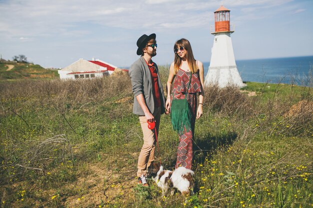 Casal jovem e elegante hippie apaixonado, caminhando com um cachorro no campo