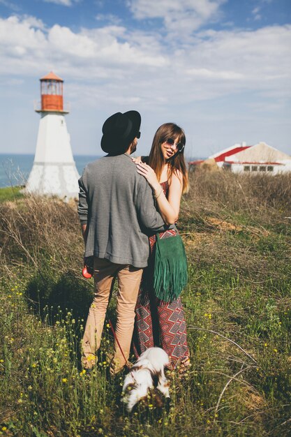 Casal jovem e elegante hippie apaixonado, caminhando com um cachorro no campo