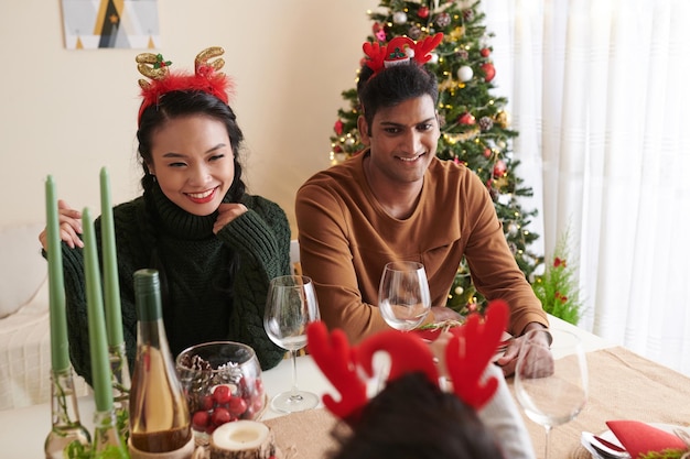 Casal jovem e feliz com chifres de rena, desfrutando do jantar de natal com a família