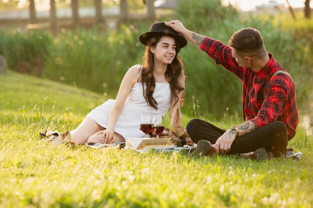 Casal jovem e feliz, desfrutando de um piquenique espalhado na beira do parque em dia de verão