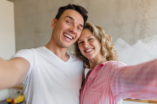 Casal jovem e fofo se divertindo no quarto pela manhã, um homem e uma mulher fazendo selfie de pijama