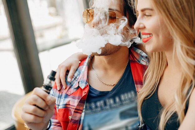 Casal jovem elegante com vape em um café