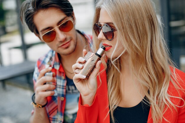 Casal jovem elegante com vape em uma cidade