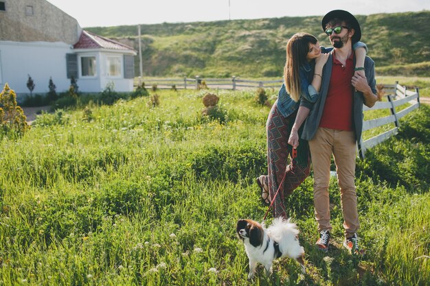 Casal jovem elegante e hippie apaixonado, caminhando com um cachorro no campo