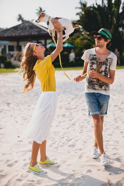 Casal jovem elegante e moderno apaixonado, andando e brincando com o cachorro na praia