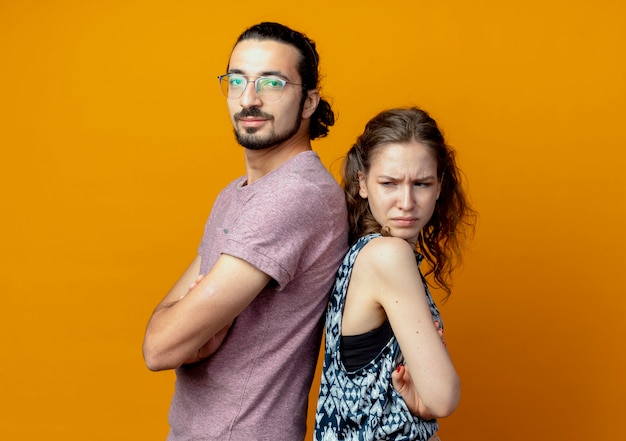 Foto grátis casal jovem em pé de costas um para o outro com os braços cruzados na parede laranja