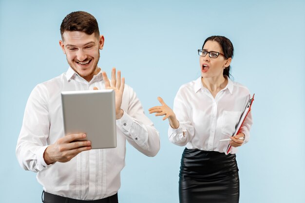 Casal jovem feliz animado, olhando para a câmera com prazer. Empresário e mulher isolados no fundo azul do estúdio