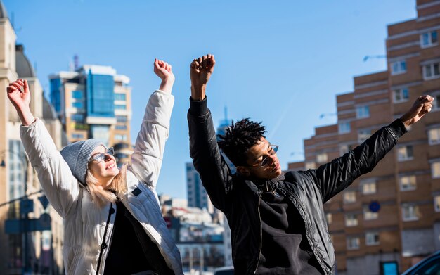 Casal jovem feliz, levantando as mãos dançando contra edifícios