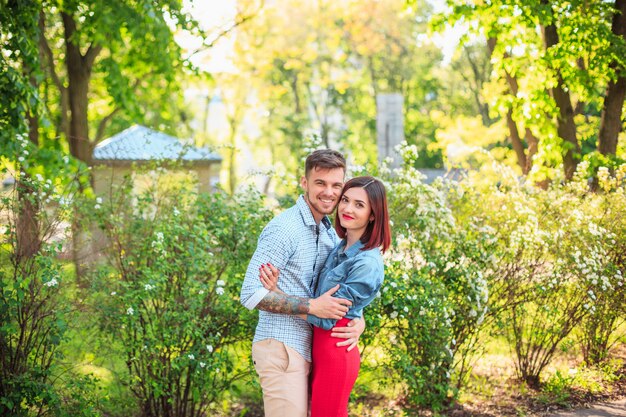 Casal jovem feliz no parque em pé e rindo no dia ensolarado