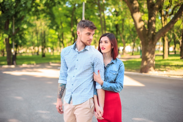 Casal jovem feliz no parque em pé e rindo no dia ensolarado