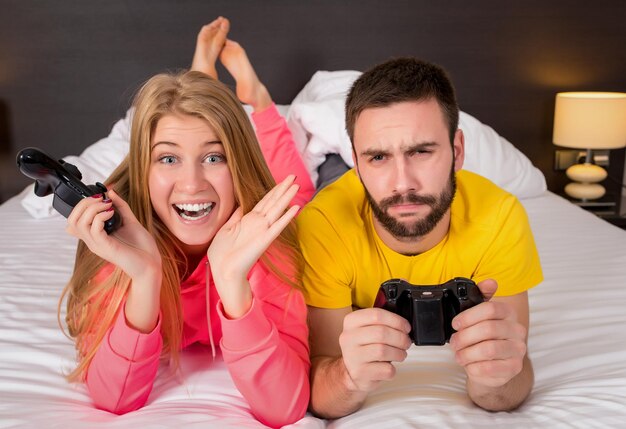 Casal jovem feliz se divertindo jogando videogame na cama.