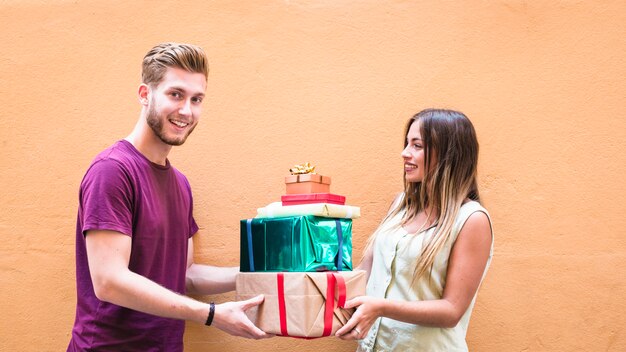 Casal jovem feliz segurando a pilha de presentes contra fundo laranja