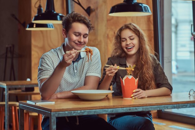 Casal jovem feliz vestindo roupas casuais comendo macarrão picante em um restaurante asiático.