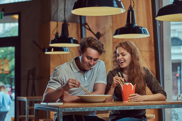 Casal jovem feliz vestindo roupas casuais comendo macarrão picante em um restaurante asiático.