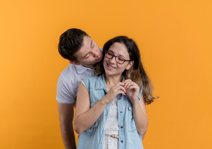 Foto grátis casal jovem, homem e mulher com roupas casuais, juntos, homem vai beijar sua amada namorada sorridente na parede laranja