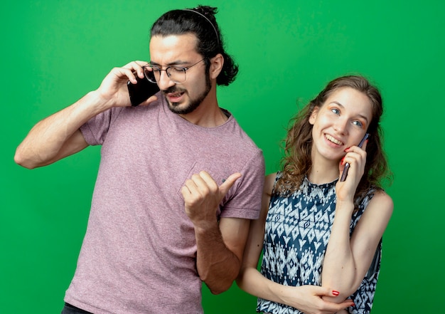 Casal jovem, homem e mulher, felizes e positivos falando em telefones celulares, em pé sobre fundo verde