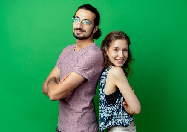 casal jovem, homem e mulher, sorrindo em pé de costas um para o outro na parede verde