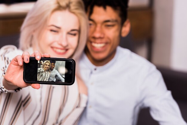 Casal jovem interracial desfocado, tendo selfie no smartphone