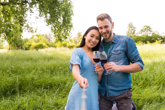 Casal jovem multirracial tomando selfie com taças de vinho