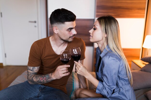 Casal jovem sentado na cama, brindando vinho