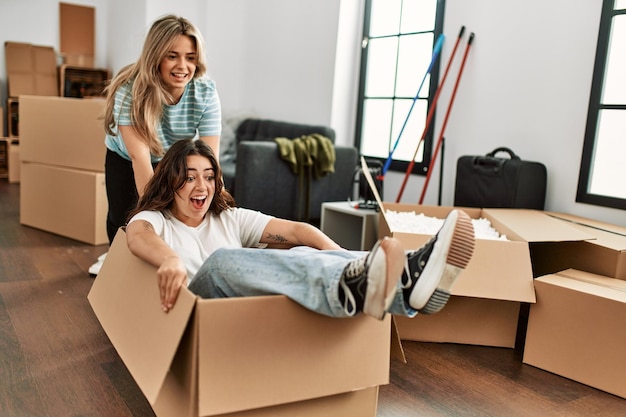 Foto grátis casal jovem sorrindo feliz brincando usando caixa de papelão como carro na nova casa