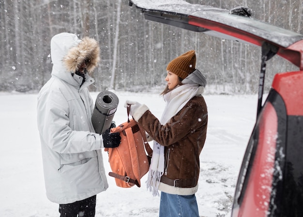 Casal jovem tirando coisas do porta-malas do carro durante uma viagem de inverno