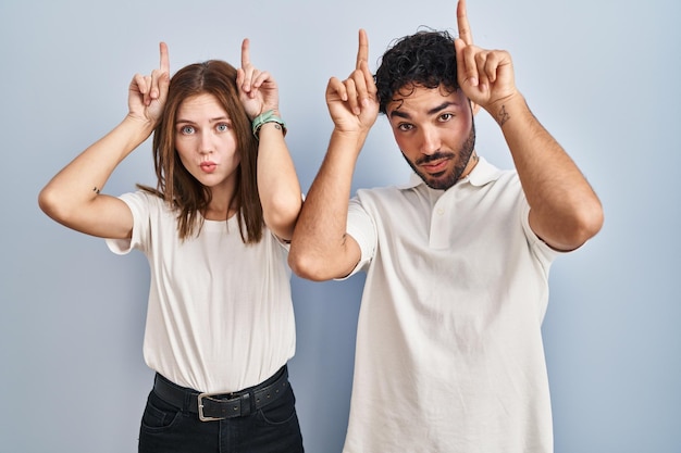 Foto grátis casal jovem vestindo roupas casuais juntos fazendo gesto engraçado com o dedo sobre a cabeça como chifres de touro