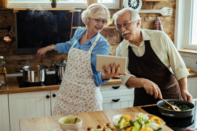 Foto grátis casal maduro seguindo receita no tablet digital enquanto prepara o almoço na cozinha